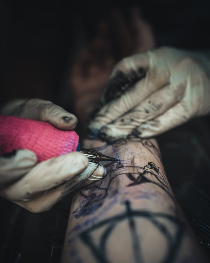 Close-up of a tattoo artist working on a client's arm, focused on hand movements and ink.